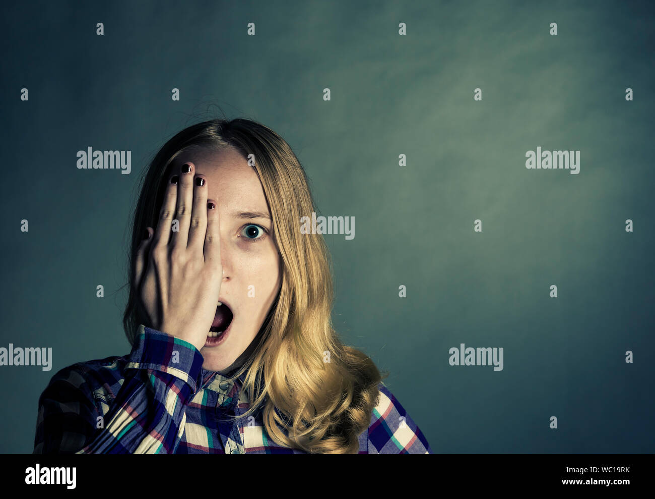 Portrait Of Surprised Young Woman With Hand On Face Against Wall Stock Photo