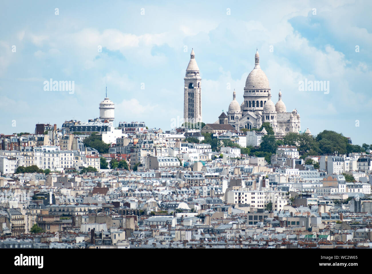 View of the Sacré-Cœur at the top of Montmartre Hill in Paris, France, on a bright cloudy day, with buildings in the foreground. Stock Photo