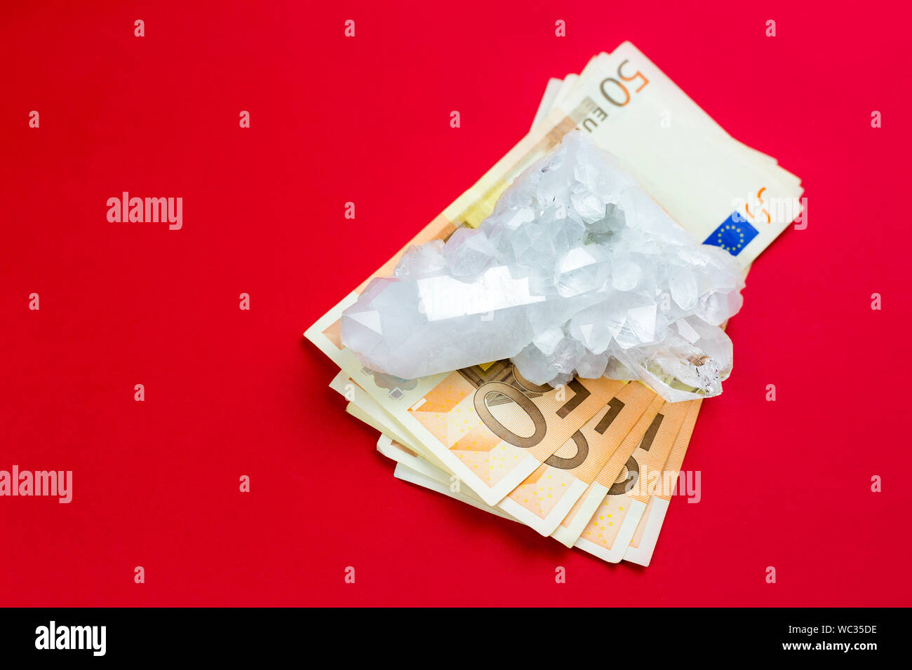 Lot of 50 euro bank notes under white pure crystal gemstone on red background. Conceptual image of business and finances in semi precious gemstone wor Stock Photo