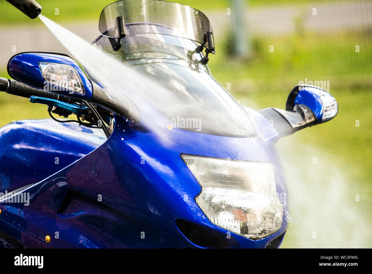 Close up view of using pressure washer to clean motorbike in home garden, green grass on background, summer day. Stock Photo