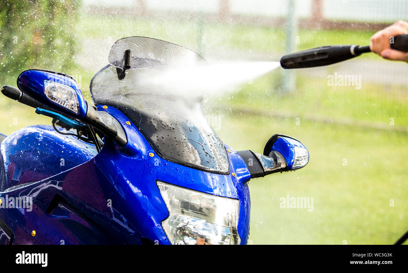 Close up view of using pressure washer to clean motorbike in home garden, green grass on background, summer day. Stock Photo