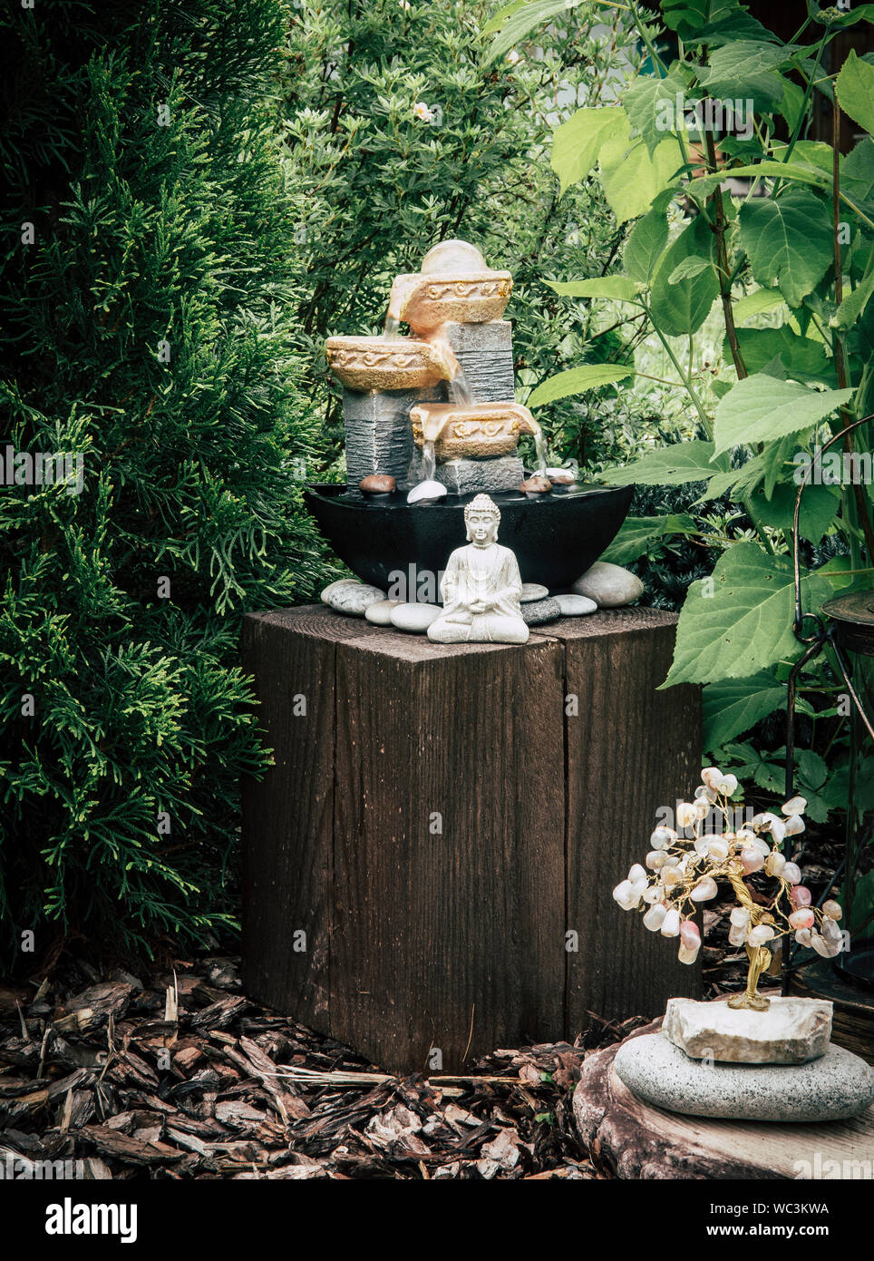 Small home garden private fountain with meditating Buddha statue between trees and bushes. Private zen garden concept. Stock Photo