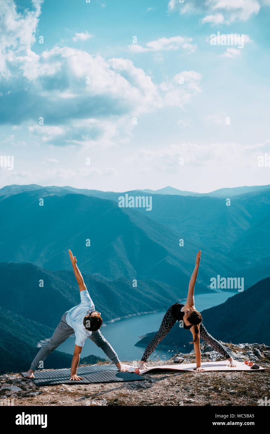 Strong and flexible young couple doing yoga workout. Man and woman on mountain practicing pair yoga in morning Stock Photo