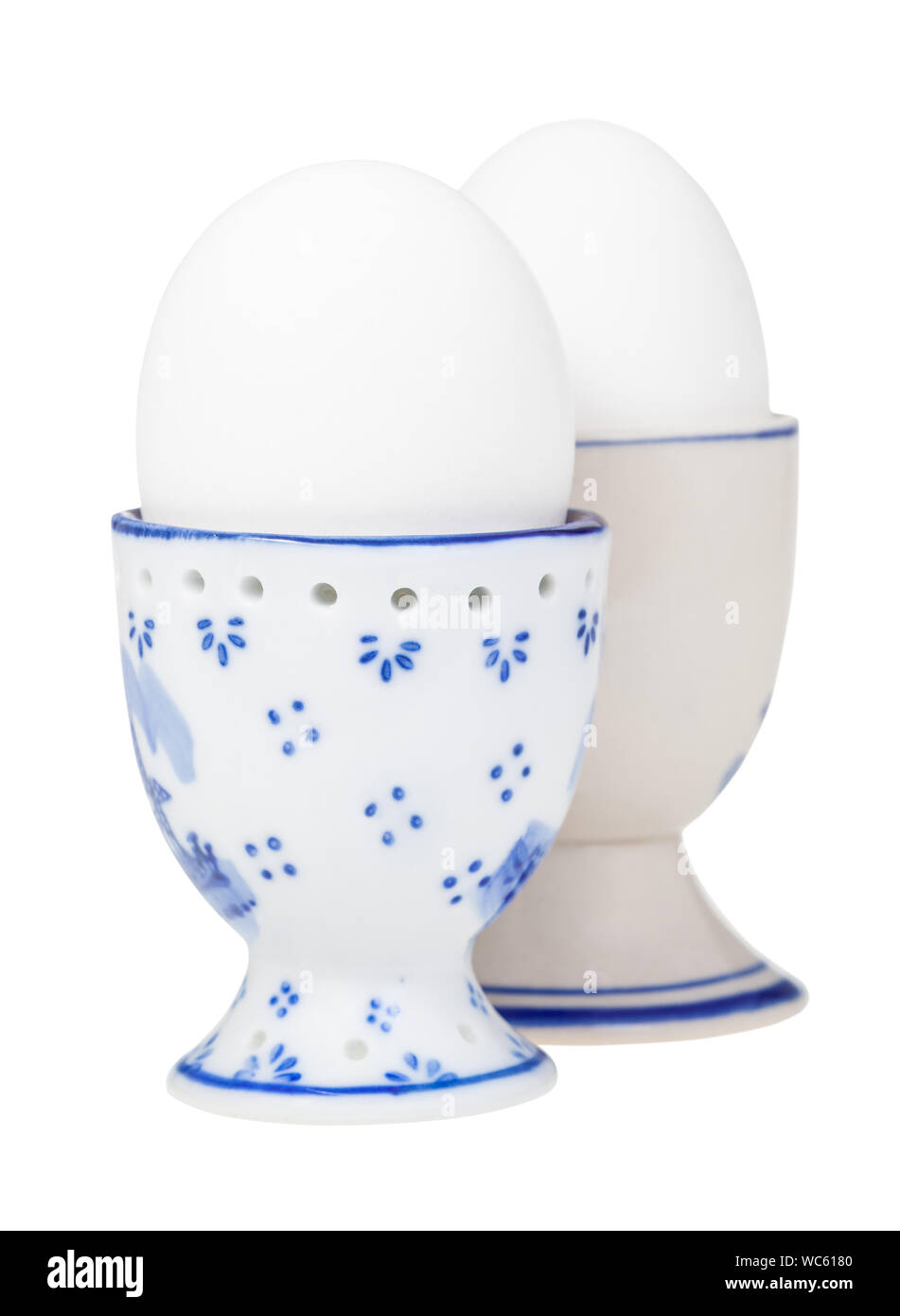side view of pair white boiled eggs in ceramic egg cups isolated on white background, the egg with a pointy end up on foreground Stock Photo