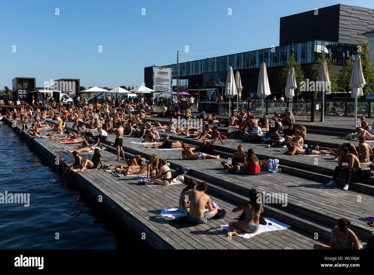 Copenhagener and tourists at the wooden pier at Ofelia Square near the Royal Play House (R) and the historic Nyhavn in Copenhagen, Denmark. The water in Copenhagen harbor is so clean that it is safe to take a dip. In 2018 Copenhagen topped CNN’s list for “Best Cities for swimming”. Stock Photo