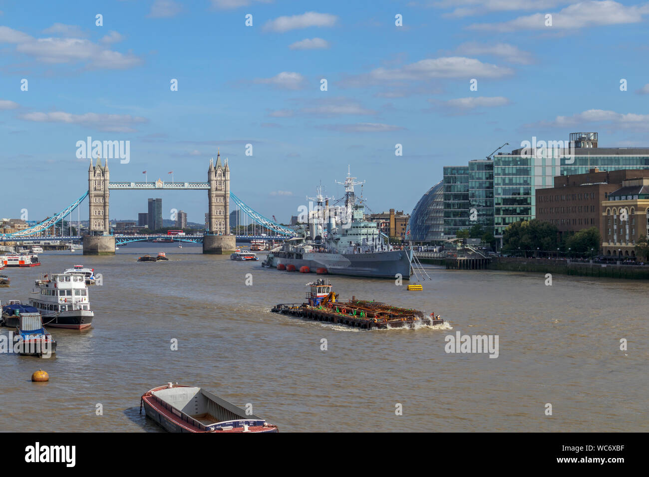 A large barge in the Pool of London on the River Thames with a view of the iconic Tower Bridge and HMS Belfast, viewed from London Bridge Stock Photo