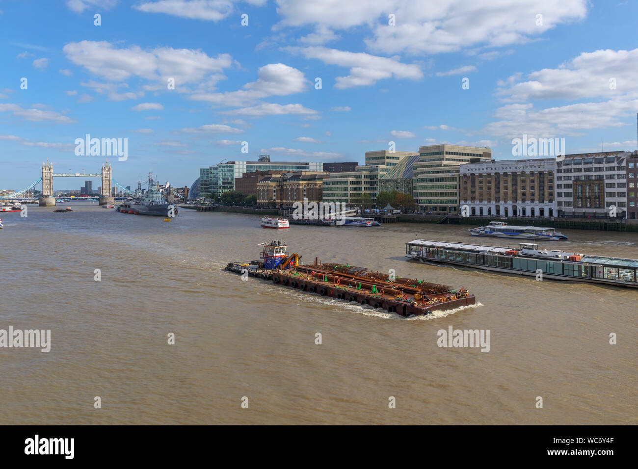 A large barge in the Pool of London on the River Thames with a view of the iconic Tower Bridge and HMS Belfast, viewed from London Bridge Stock Photo