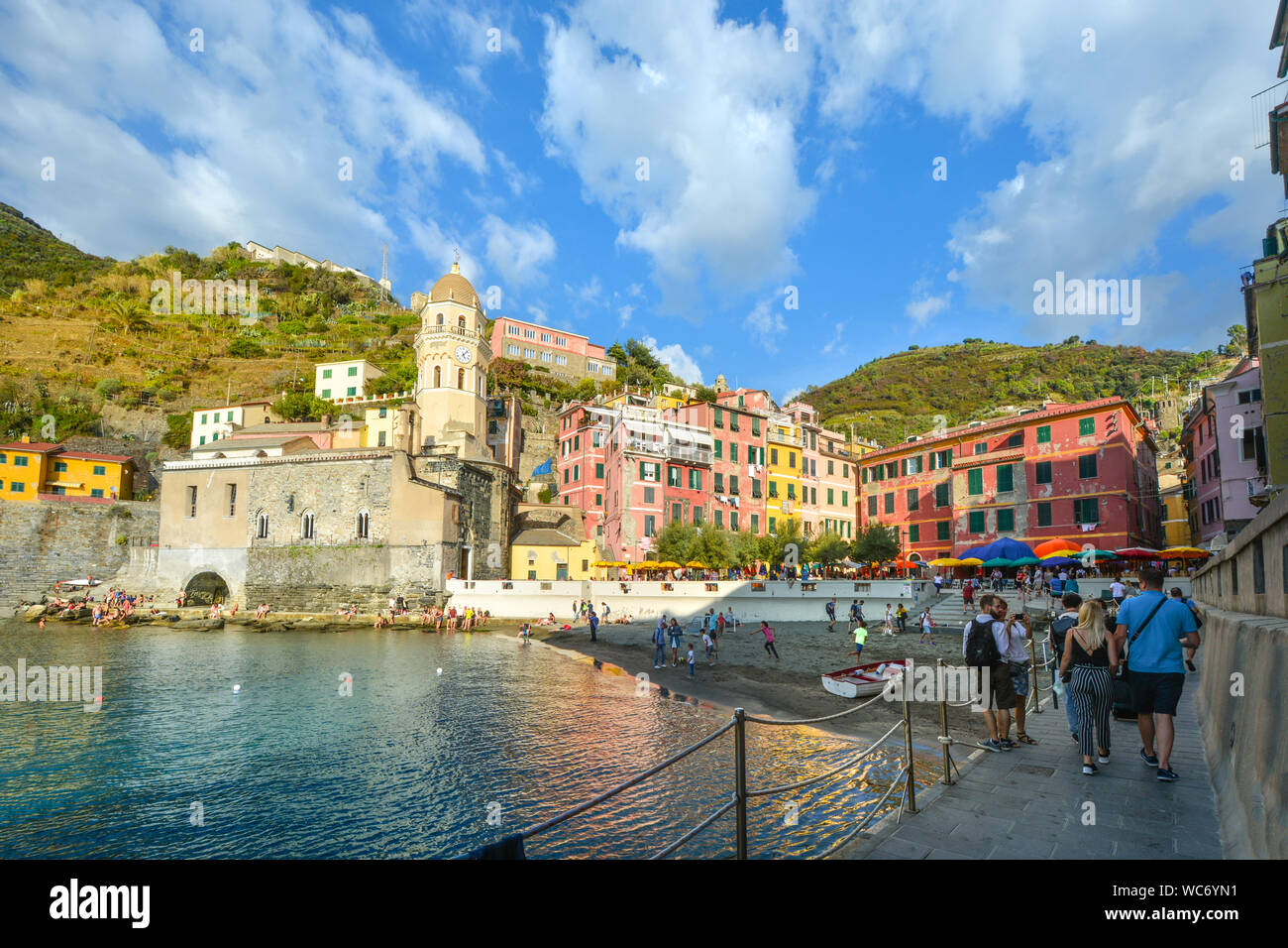 The harbour of Vernazza, Cinque Terre Italy, with kids playing on the beach, tourists enjoying the town and the church of Santa Margherita in the sun Stock Photo