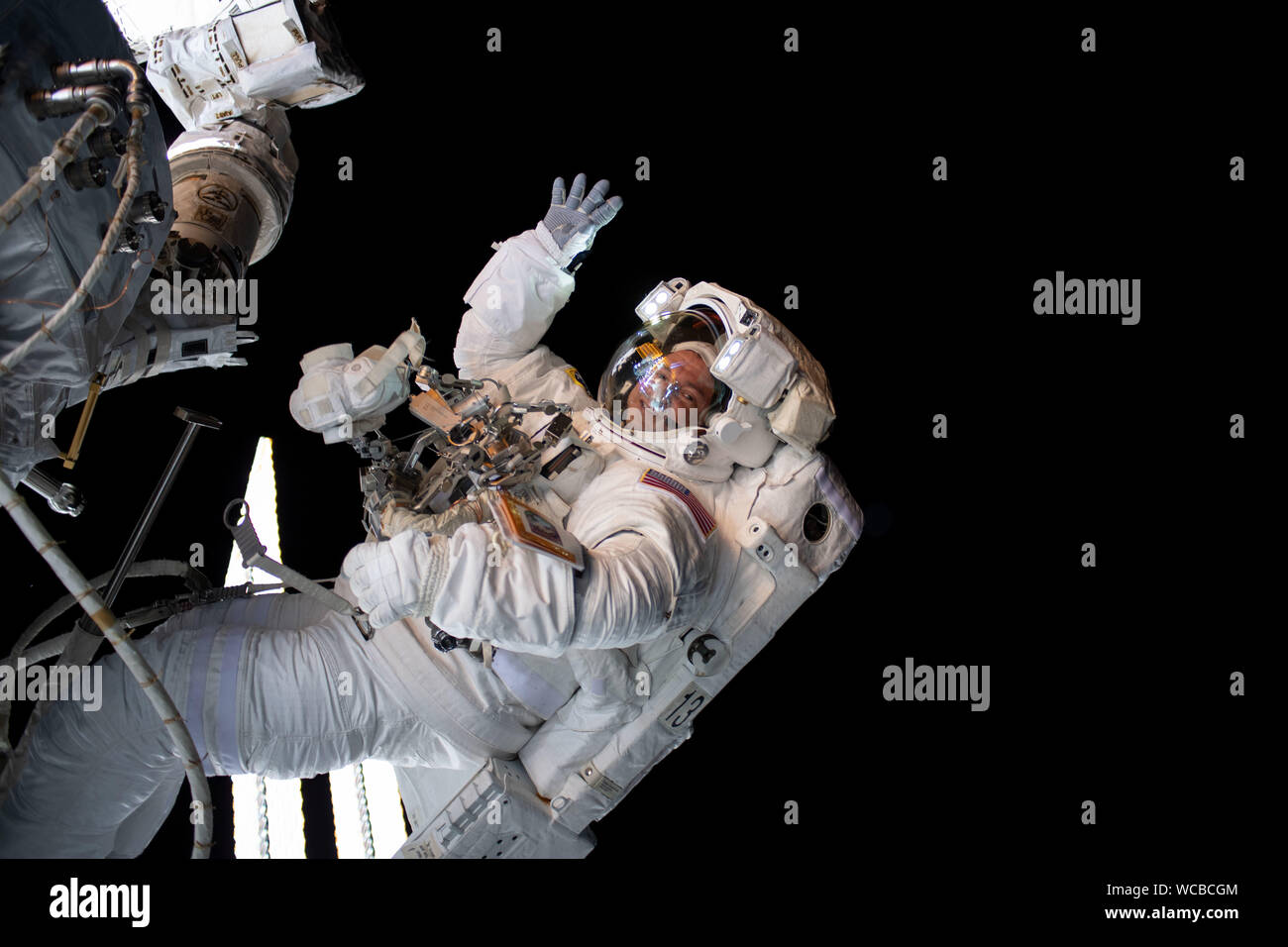 NASA astronaut Andrew Morgan waves during a spacewalk outside the International Space Station August 21, 2019 in Earth Orbit. Morgan and fellow astronaut Nick Hague spent six-hours and 32-minutes on a spacewalk to install the second commercial crew vehicle docking port, to accommodate the future arrivals of Boeing CST-100 Starliner and SpaceX Crew Dragon commercial crew spacecraft. Stock Photo