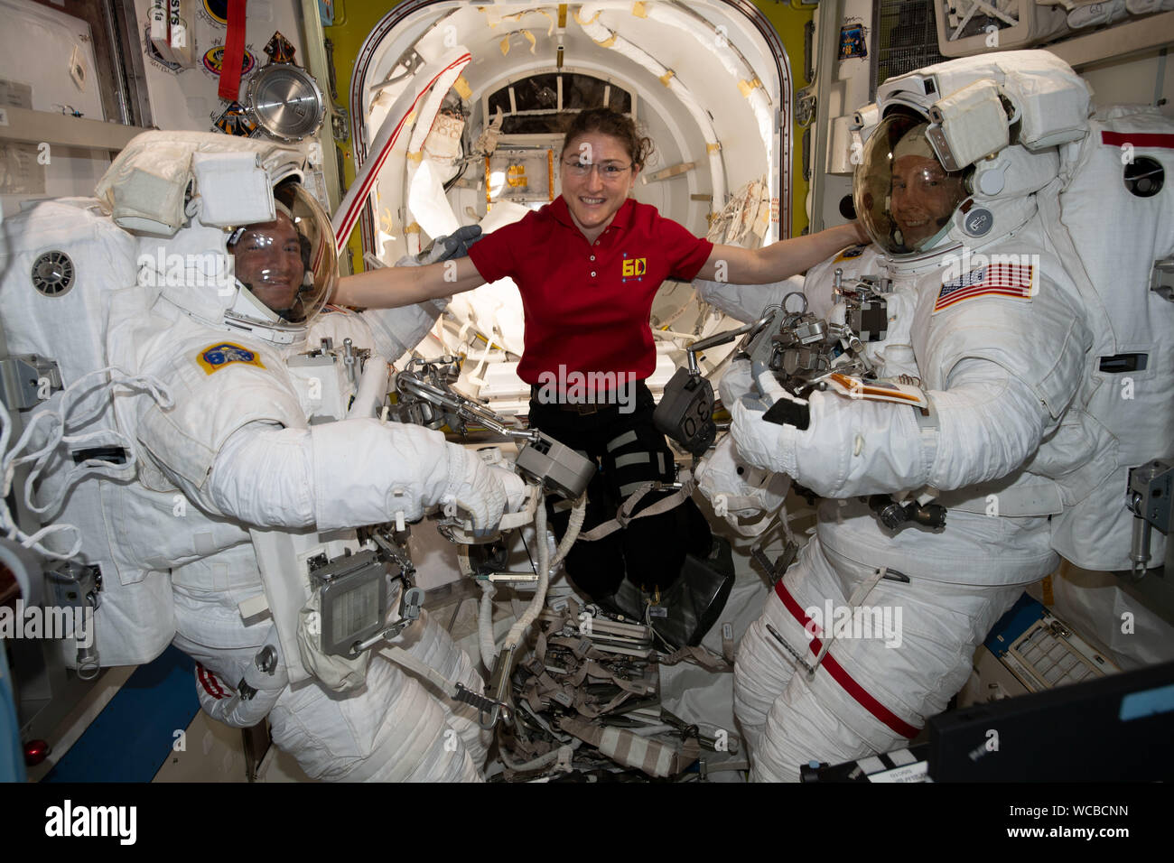 NASA astronaut Christina Koch poses with fellow astronauts Andrew Morgan and Nick Hague wearing their spacesuits in the Quest Airlock onboard the International Space Station August 21, 2019 in Earth Orbit. Morgan and Hague spent six-hours and 32-minutes on a spacewalk to install the second commercial crew vehicle docking port, to accommodate the future arrivals of Boeing CST-100 Starliner and SpaceX Crew Dragon commercial crew spacecraft. Stock Photo
