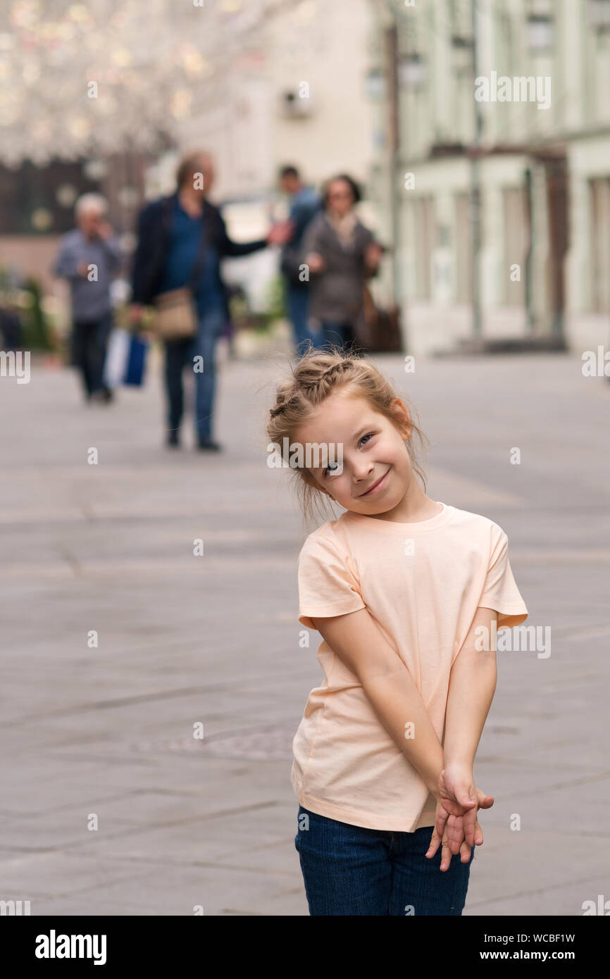 Cute little naughty girl walking through the city streets and posing for the camera. Time of prank. Urban casual outfit. Carefree. Happiness, fun and Stock Photo