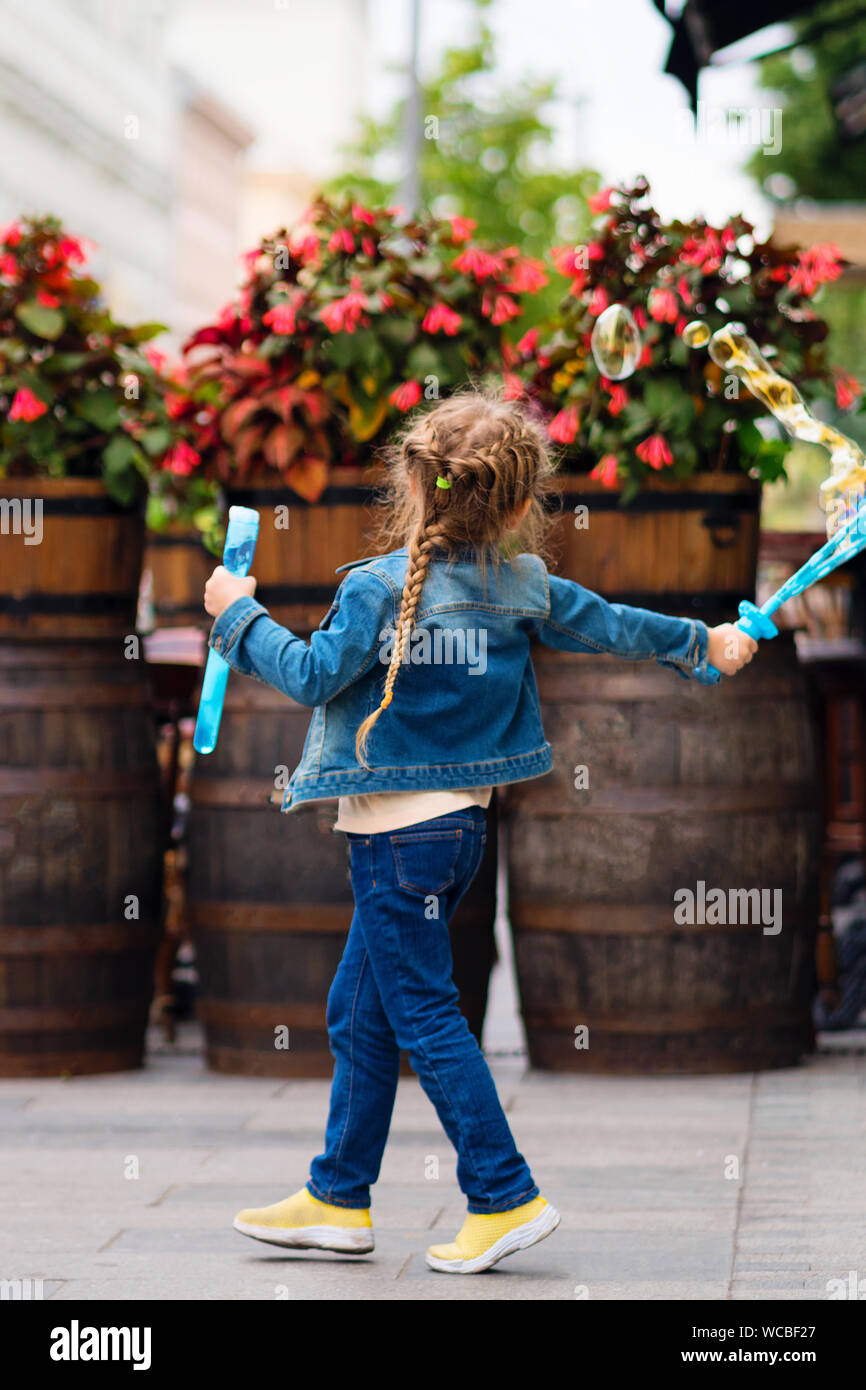 Adorable little girl having fun outdoors, blowing bubbles in city street. Carefree time. Happiness, fun and childhood concept. Stock Photo