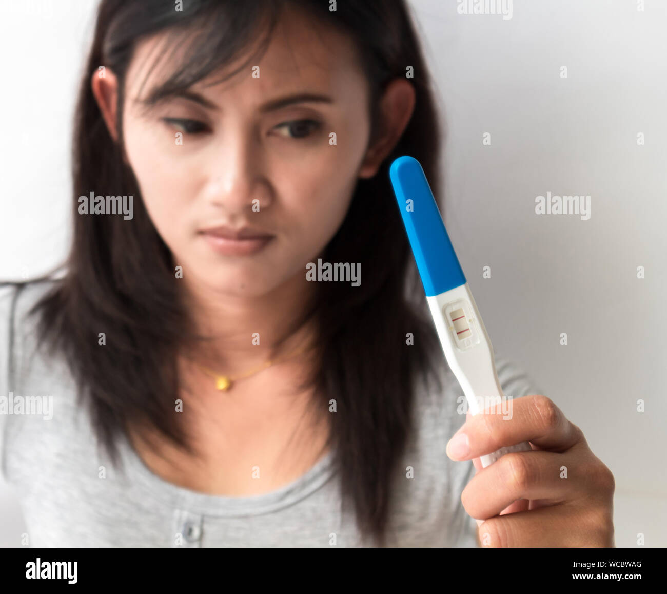 Upset Woman Holding Positive Pregnancy Test Result Against Wall Stock Photo