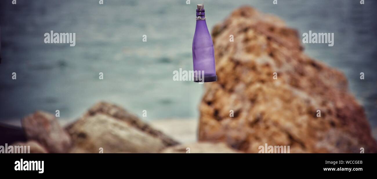 Glass Bottle Hanging Against Rocks On Sea Shore Stock Photo