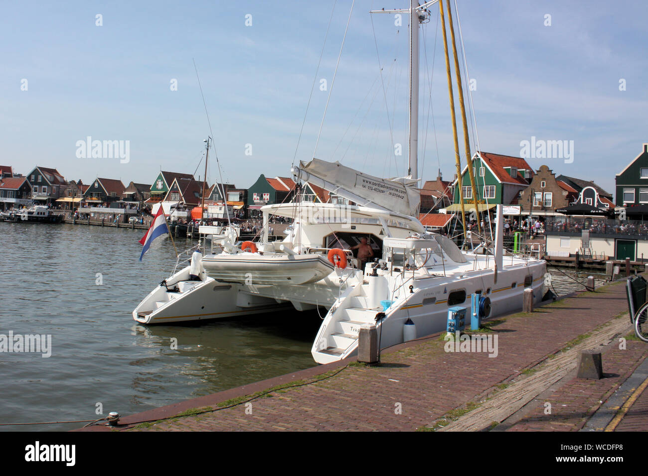 A sport yacht is docking at the pier in front of the fisherman traditional wooden houses in Volendam village on a sunny day. Stock Photo