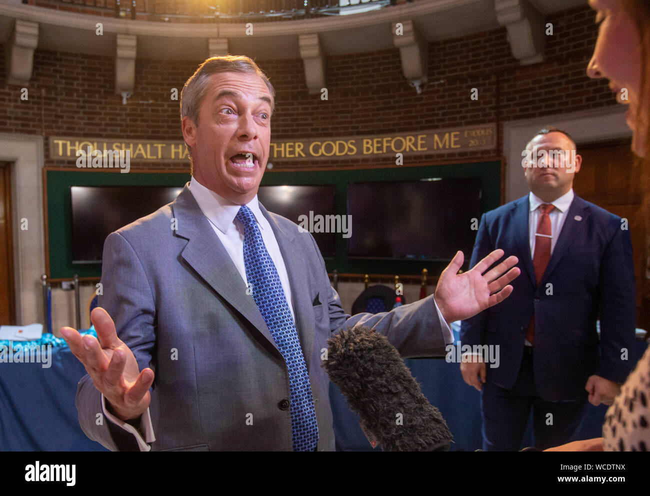 Brexit Party Leader, Nigel Farage, gives a press interview with one of the Ten commandments 'Thou shalt have no other Gods before me' on the wall in t Stock Photo