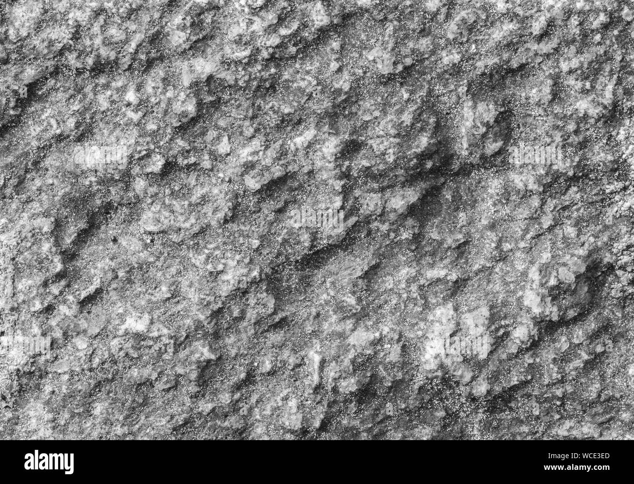 Macro close-up of a rough rock surface with fine grains of sand in black and white. High resolution full frame textured background. Stock Photo