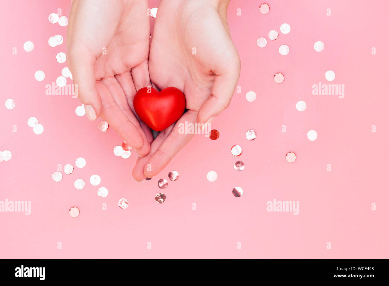 Woman's hands with manicure hold red heart on pale pink background with ...