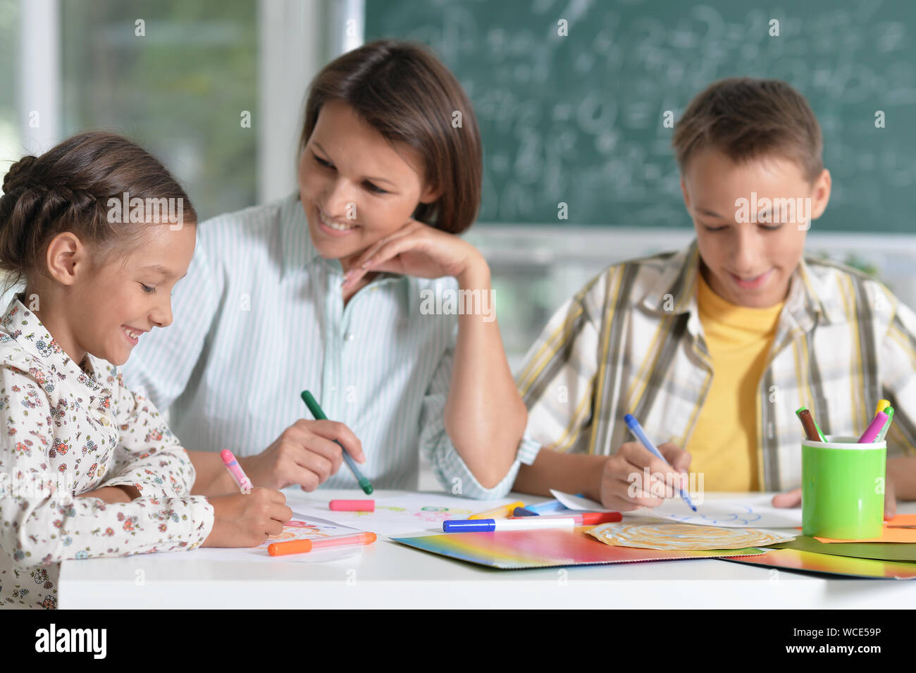 Children at school sitting in the classroom with teacher and painting ...