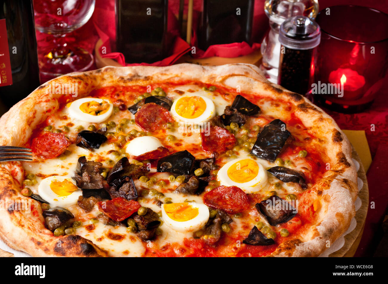 Italian pizza with fried eggplants, hot salami, eggs and green peas