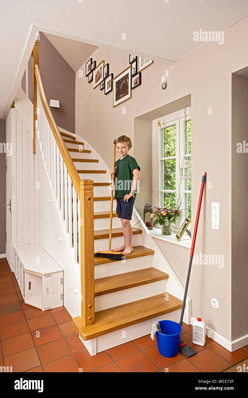 Boy, 8 years, helping at home in the household, sweeping the stairs with a broom. Stock Photo
