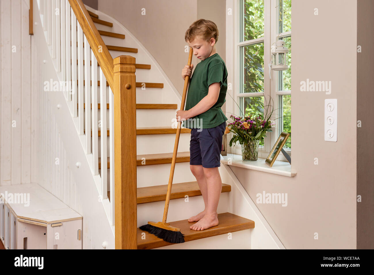 Boy, 8 years, helping at home in the household, sweeping the stairs