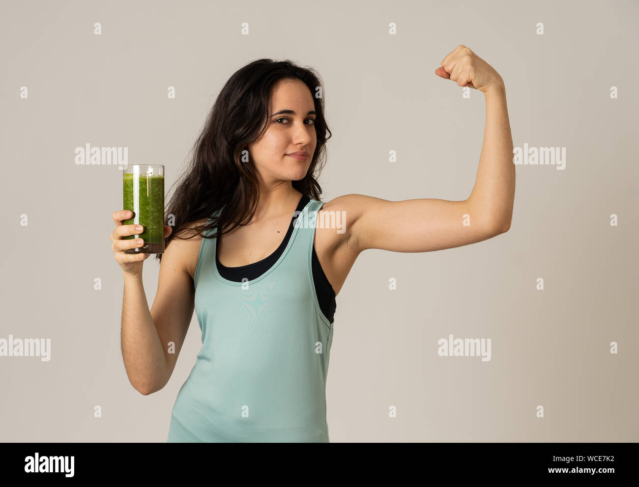 Fitness woman happy smiling holding glass of green vegetable smoothie posing happy and cute after training exercise felling fit and strong. In Body ca Stock Photo