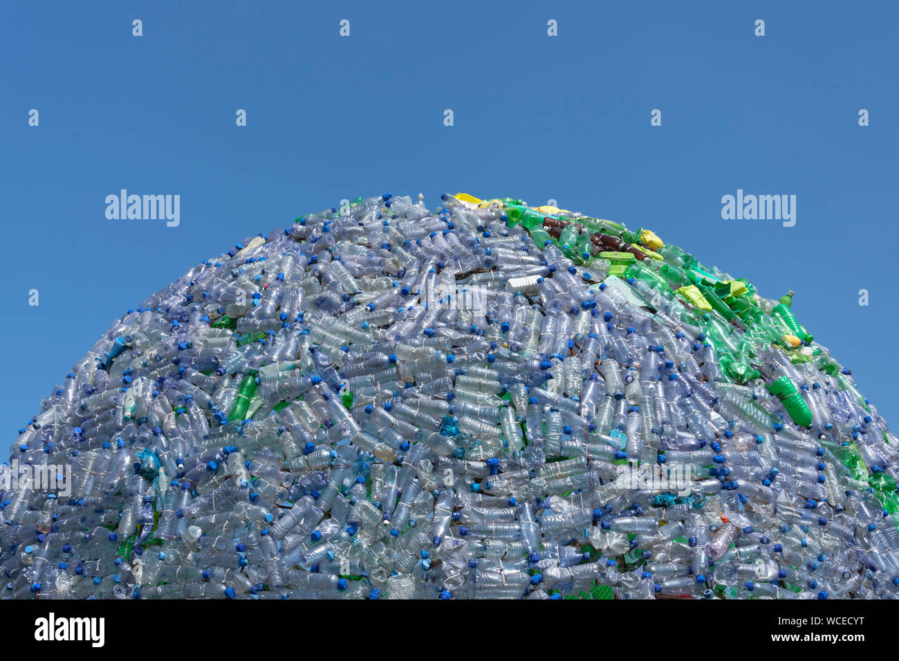 Half globe made of blue and green plastic waste, plastic bottles with a beautiful blue sky as background Stock Photo