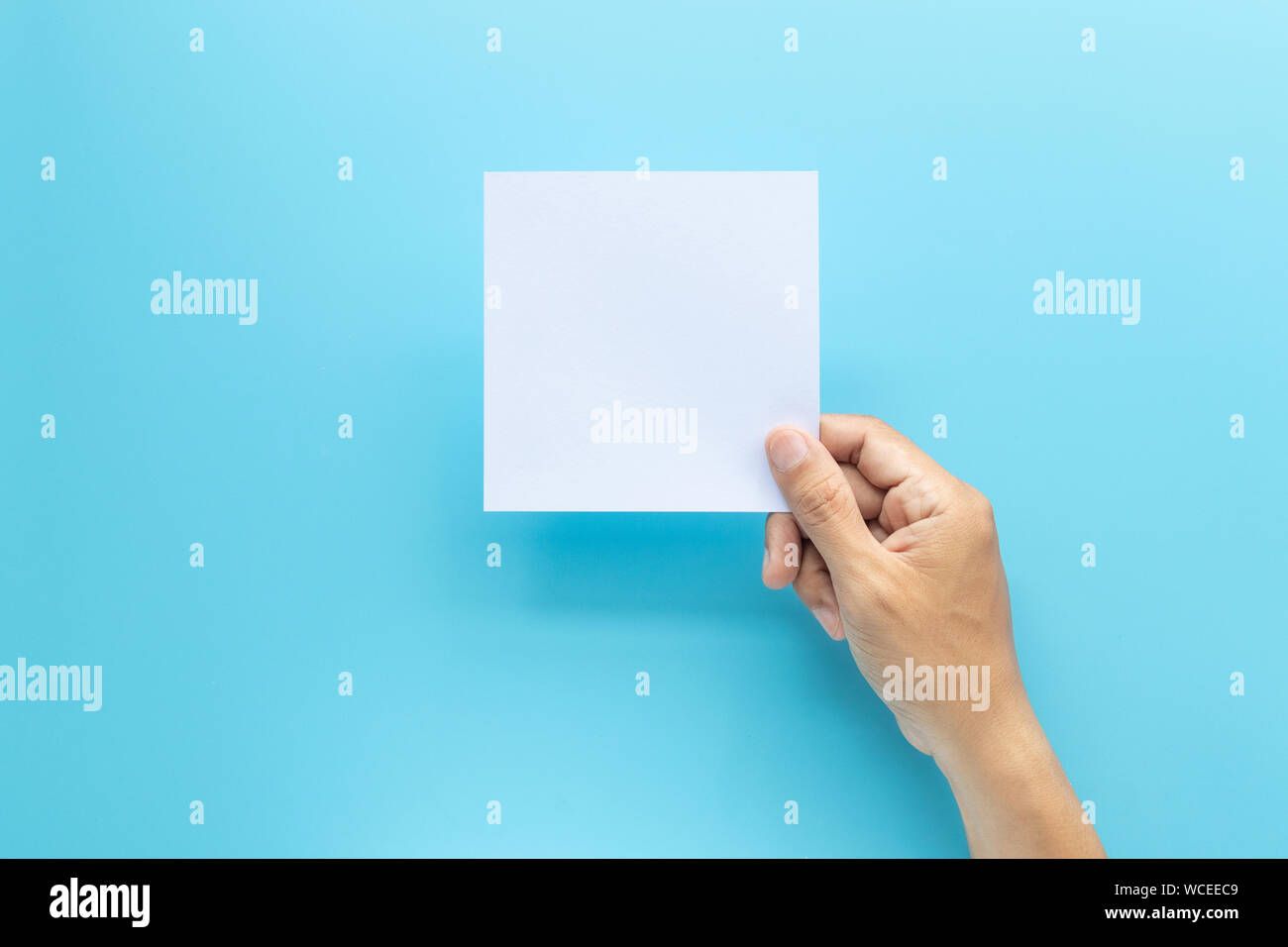 man hand holding blank card paper sheet isolated on blue background with copy space. Stock Photo