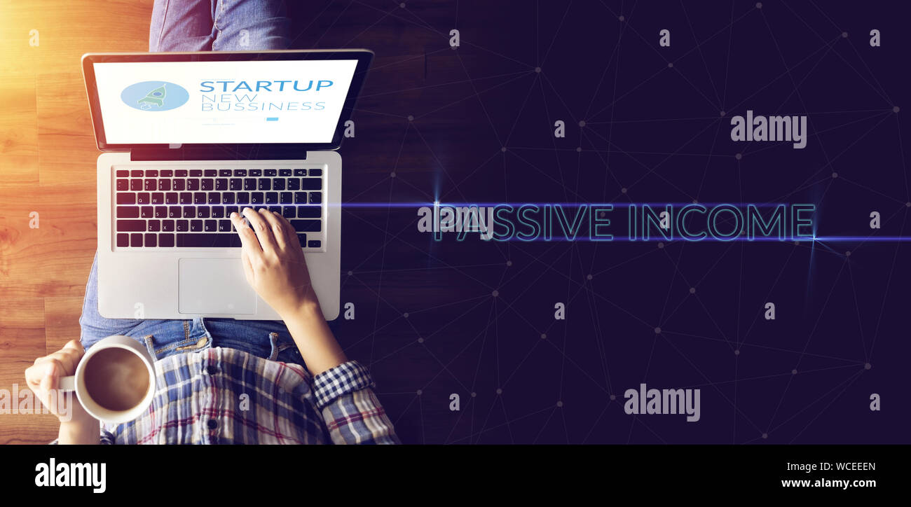 top view of people working on notebook laptop computer from home on wooden floor with startup business and rocket logo on screen and text passive inco Stock Photo