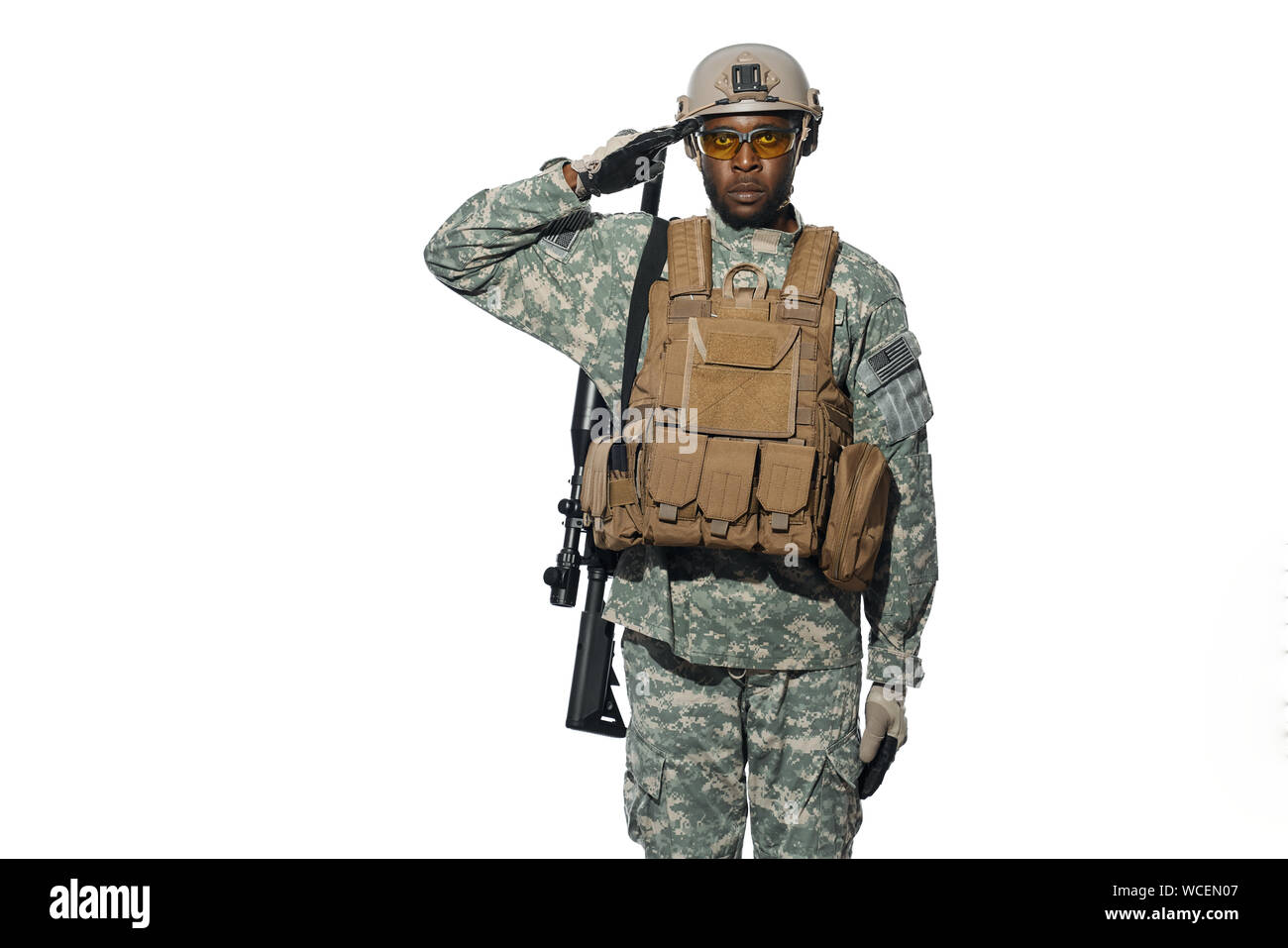 Front view of African male soldier serve in army, hears and executes orders. American soldier wearing uniform with modern weapon machine holding hand near head. White studio background. Stock Photo