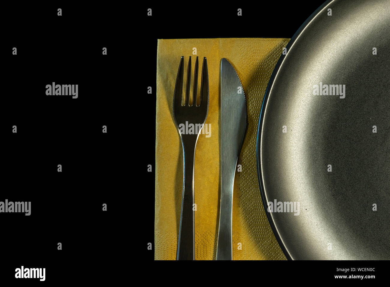 metal fork, knife on yellow napkin and plate on a black background. top