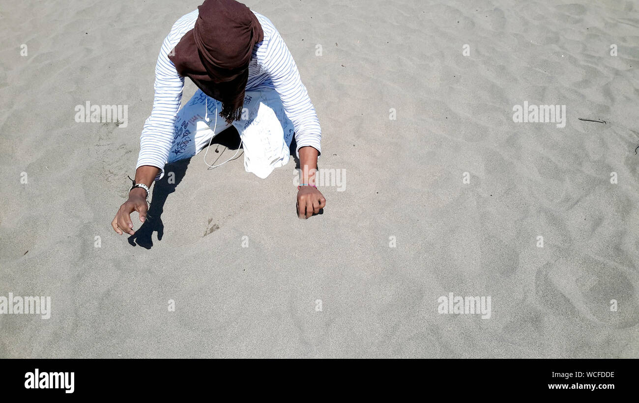 Unrecognizable Person Kneeling On Sand Stock Photo