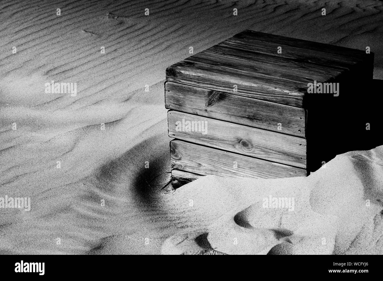 a wooden box being consumed by the sands at Tarifa, Spain in black and white Stock Photo