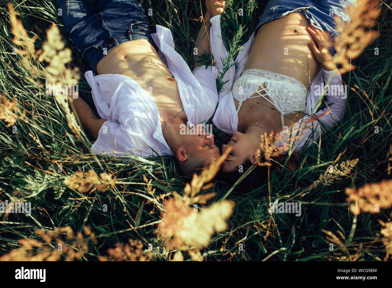 Happy couple with pregnant woman lies on the meadow among grass during a walk. Top view. Stock Photo