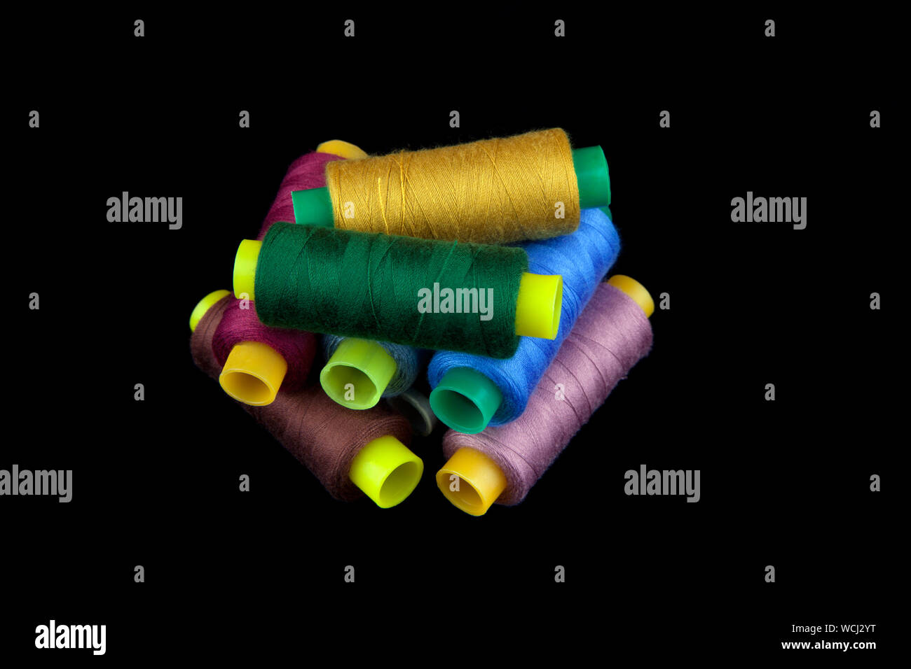 Reels of colourful threads stacked against a black background. Stock Photo