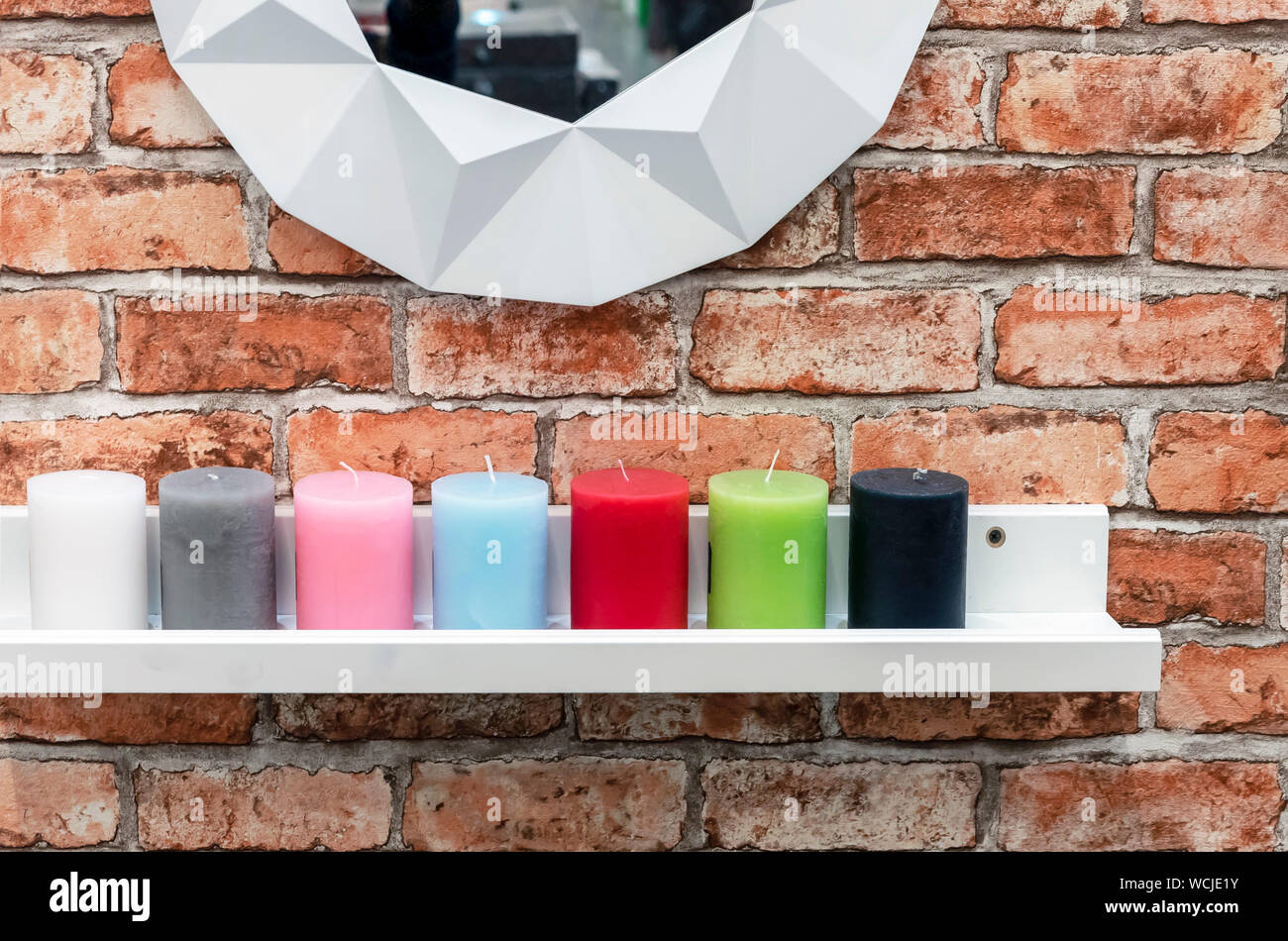 Candles of different colors are on the white shelf in the loft interior. Stock Photo