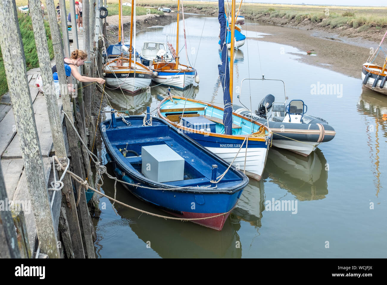 People crabbing on quayside, River Glaven, Blakeney, Norfolk alongside moored small boats Stock Photo