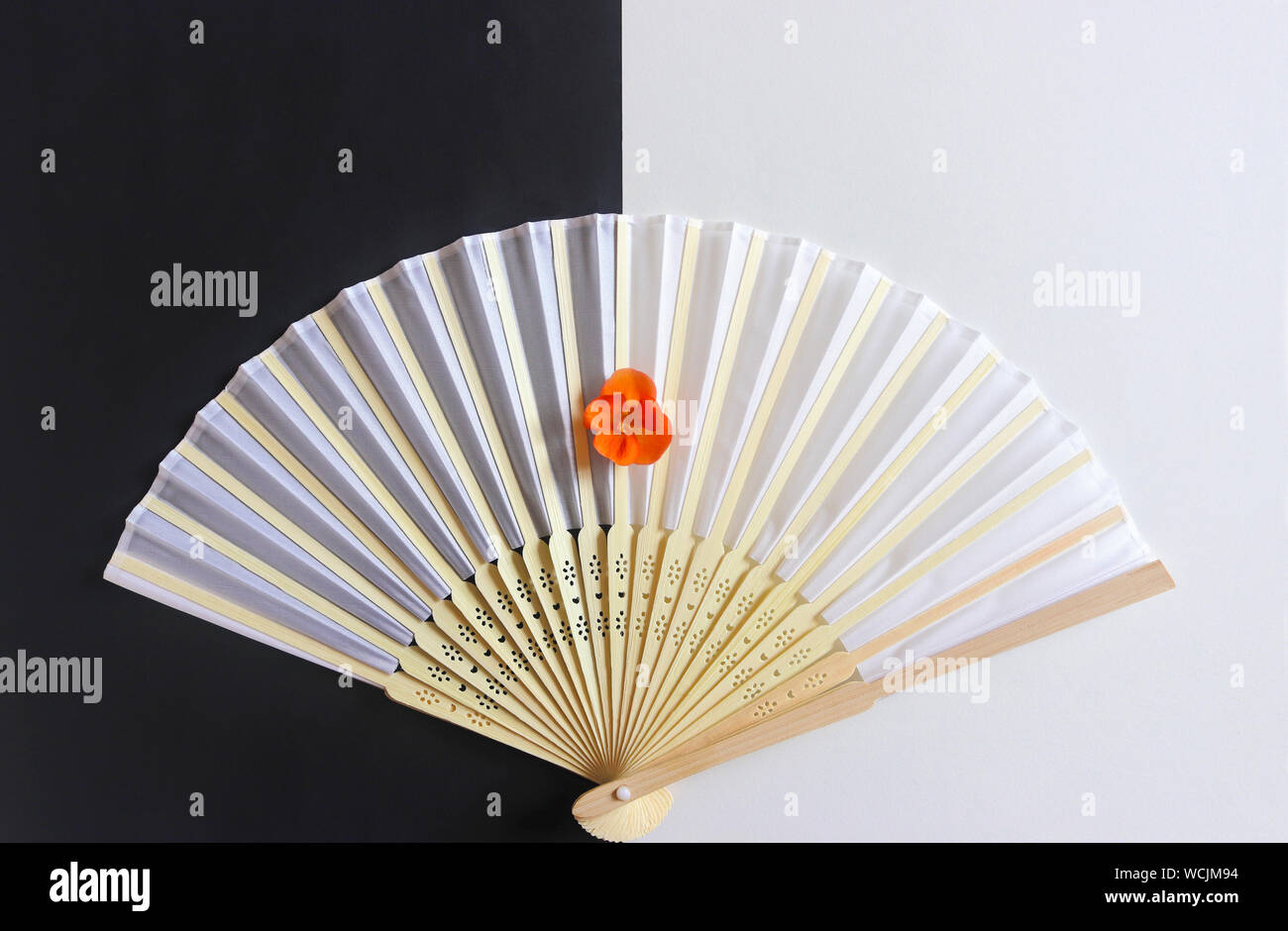 decorative white hand fan with a wooden grip and an orange colored blossom on black and white paper Stock Photo