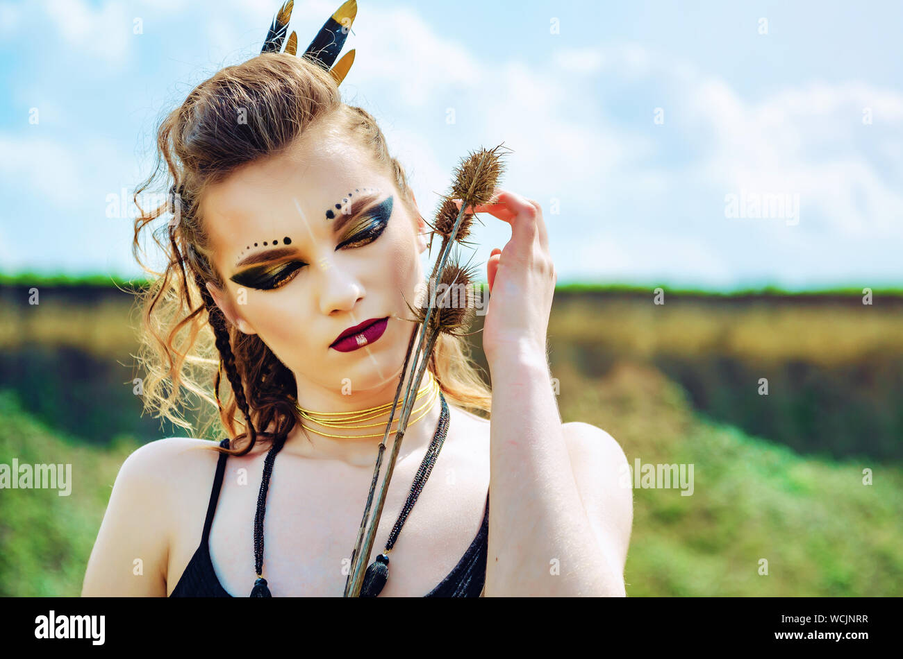 Portrait of a girl with aggressive makeup amazon viking presses prickly  flowers thistle to her face Stock Photo - Alamy