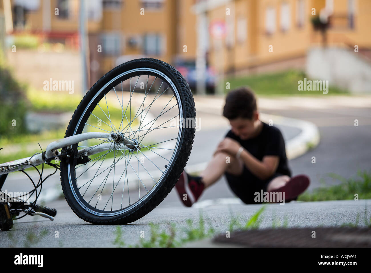 Kid hurts his leg after falling off his bicycle. Child is learning to ride a bike. Boy in the