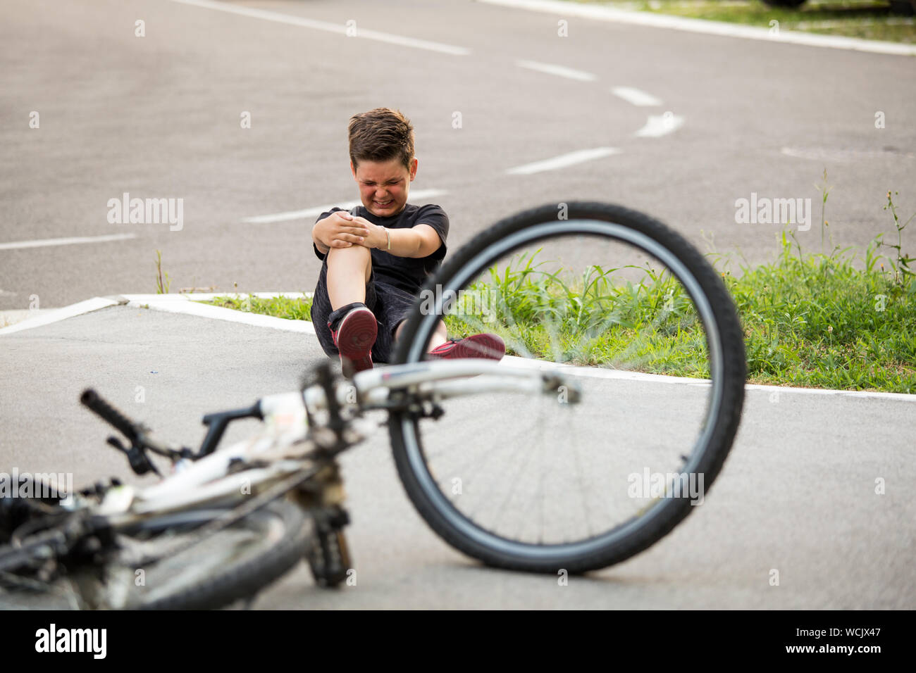 Kid hurts his leg after falling off his bicycle. Child is learning to