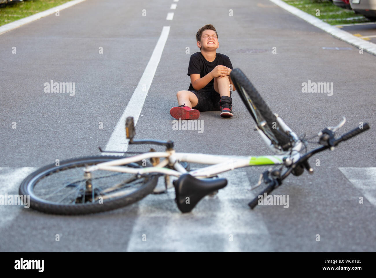 Kid hurts his leg after falling off his bicycle. Child is learning to