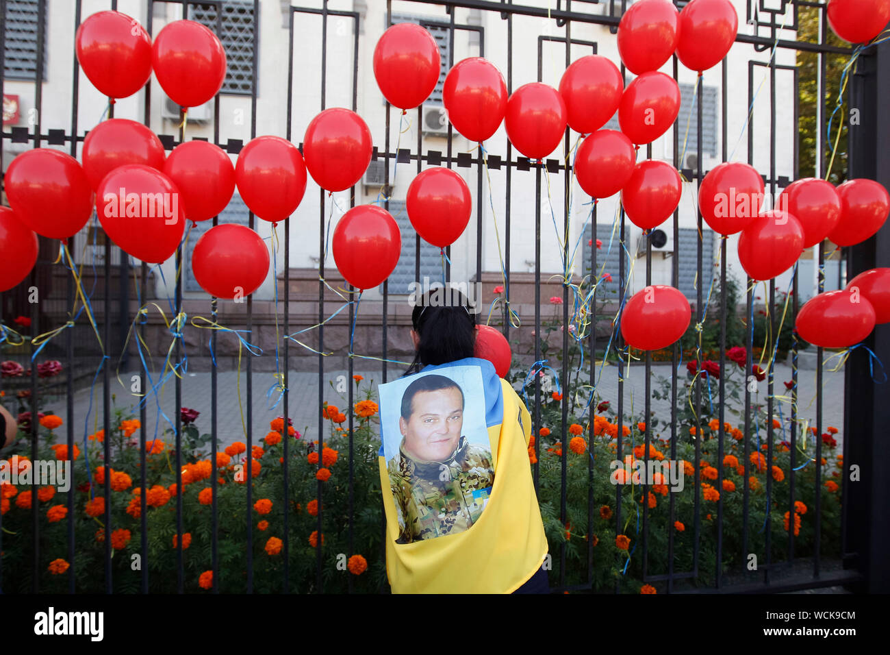 Kiev, Ukraine. 28th Aug, 2019. A woman sets up on a fence of the Russian Embassy symbolic red balloons, during a rally in Kiev.Ukrainians mark the 5th anniversary of Ilovaysk battle on the East of Ukraine, and gathered in memory of lost the Ukrainian soldiers. According to Ukraine officials, 366 Ukrainian soldiers got lost and 158 were missing during heavy fighting between Ukrainian government forces and Russian-backed separatists at the Eastern Ukraine near of Ilovaysk city on August 2014. Credit: SOPA Images Limited/Alamy Live News Stock Photo