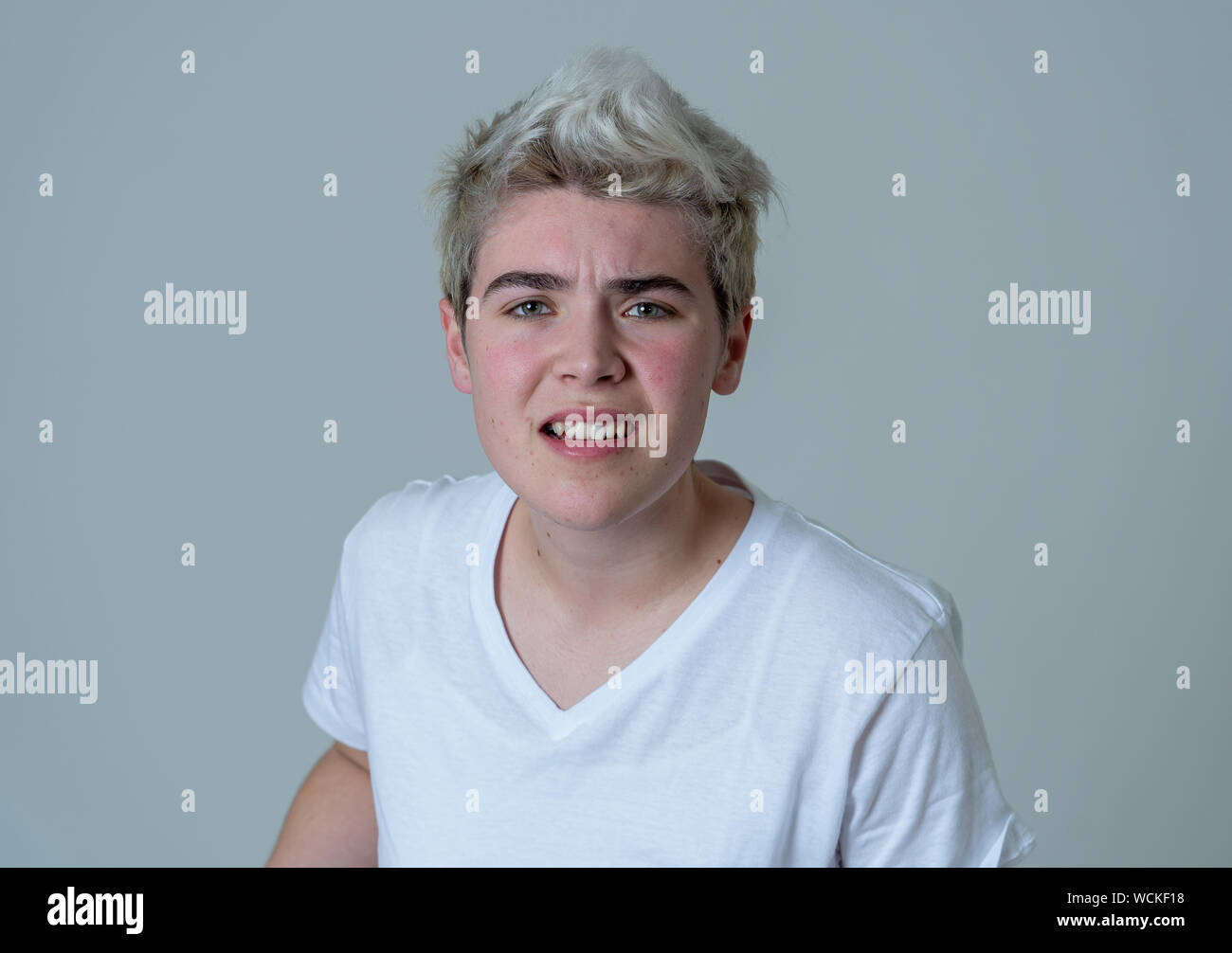 Portrait of young attractive transgender teenager man with angry face. Looking mad and furious. Facial expressions and emotions. Isolated on neutral b Stock Photo