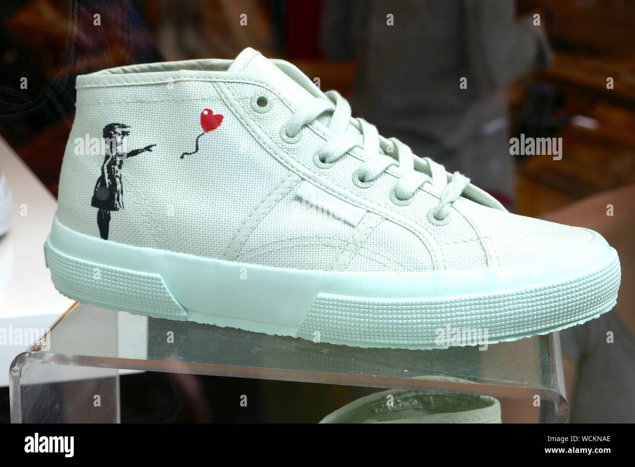 Banksy's most popular work the balloon girl painted on a pair of trainers in a shop widow in Carnaby Street . Stock Photo