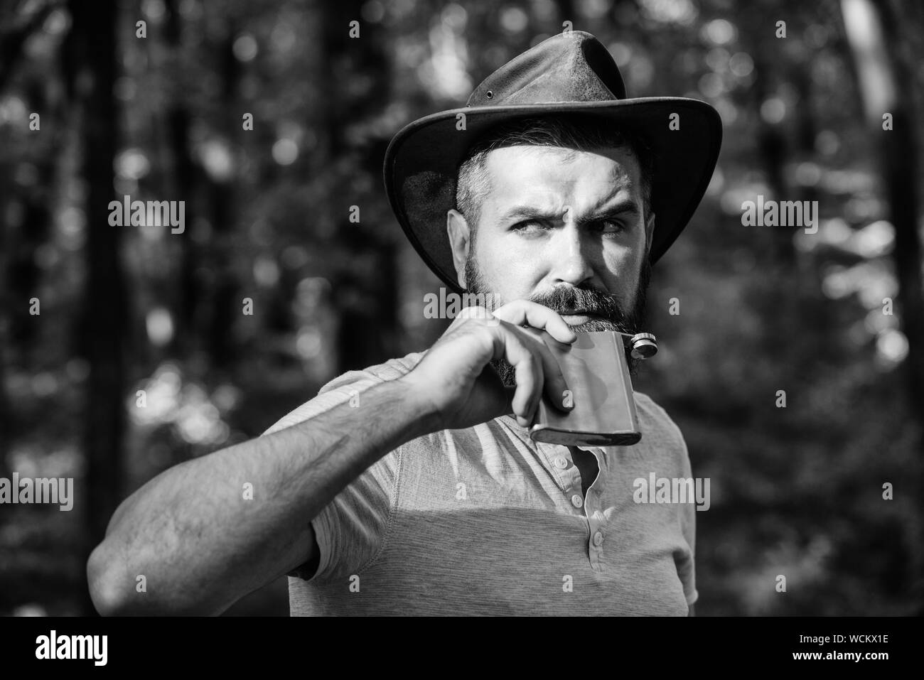 man hipster relax in autumn forest. Spring sunny weather. camping and hiking. mature male with brutal look drink alcohol from metallic flask. Bearded man in cowboy hat walk in park outdoor. Stock Photo