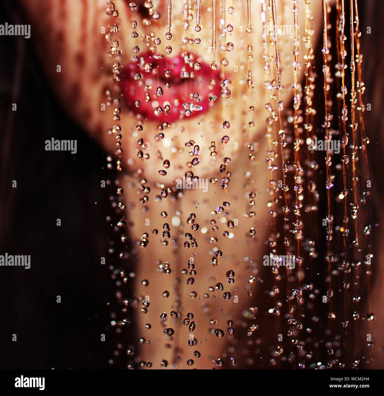 A close up of a girl's face and lips behind water droplets in the rain. Crisp texture of water droplets and blurred out face for a mystic composition. Stock Photo