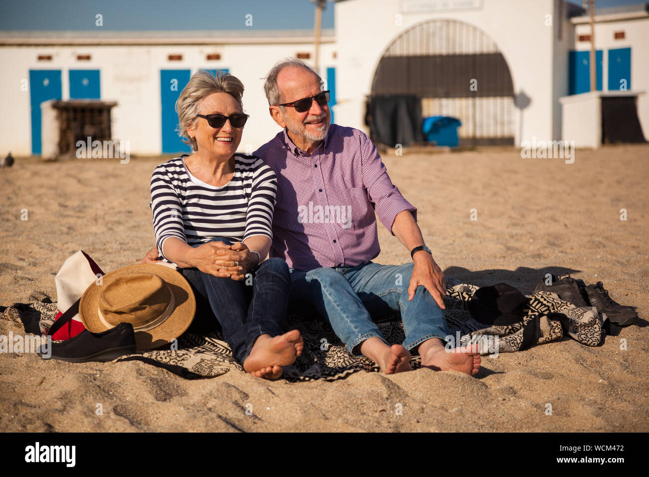 A happy senior couple sitting on the beach and enjoying the view end the sunshine Stock Photo
