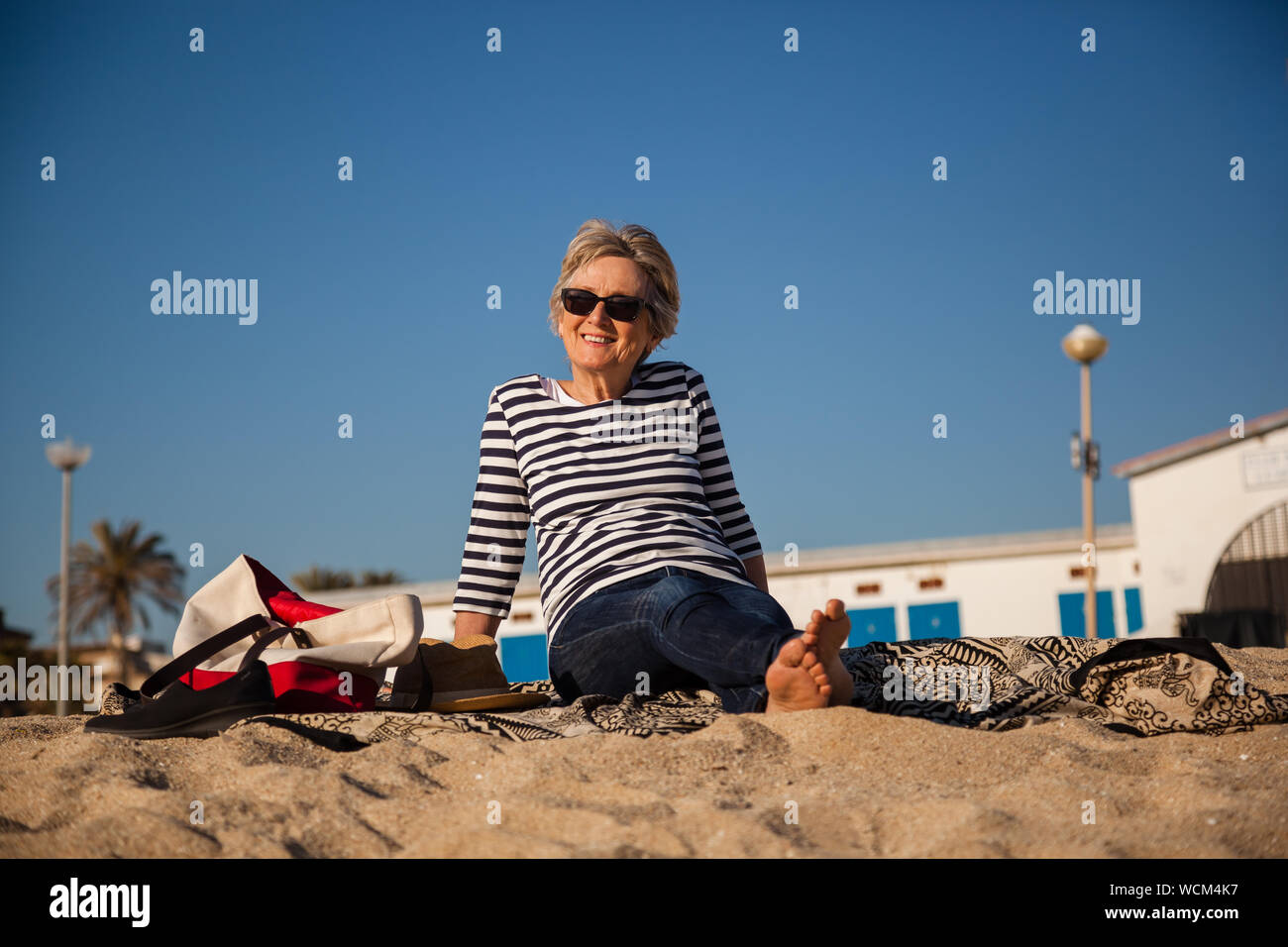 Modern elderly lady with striped t-shirt enjoying sun and beach with big blue sky in the background Stock Photo